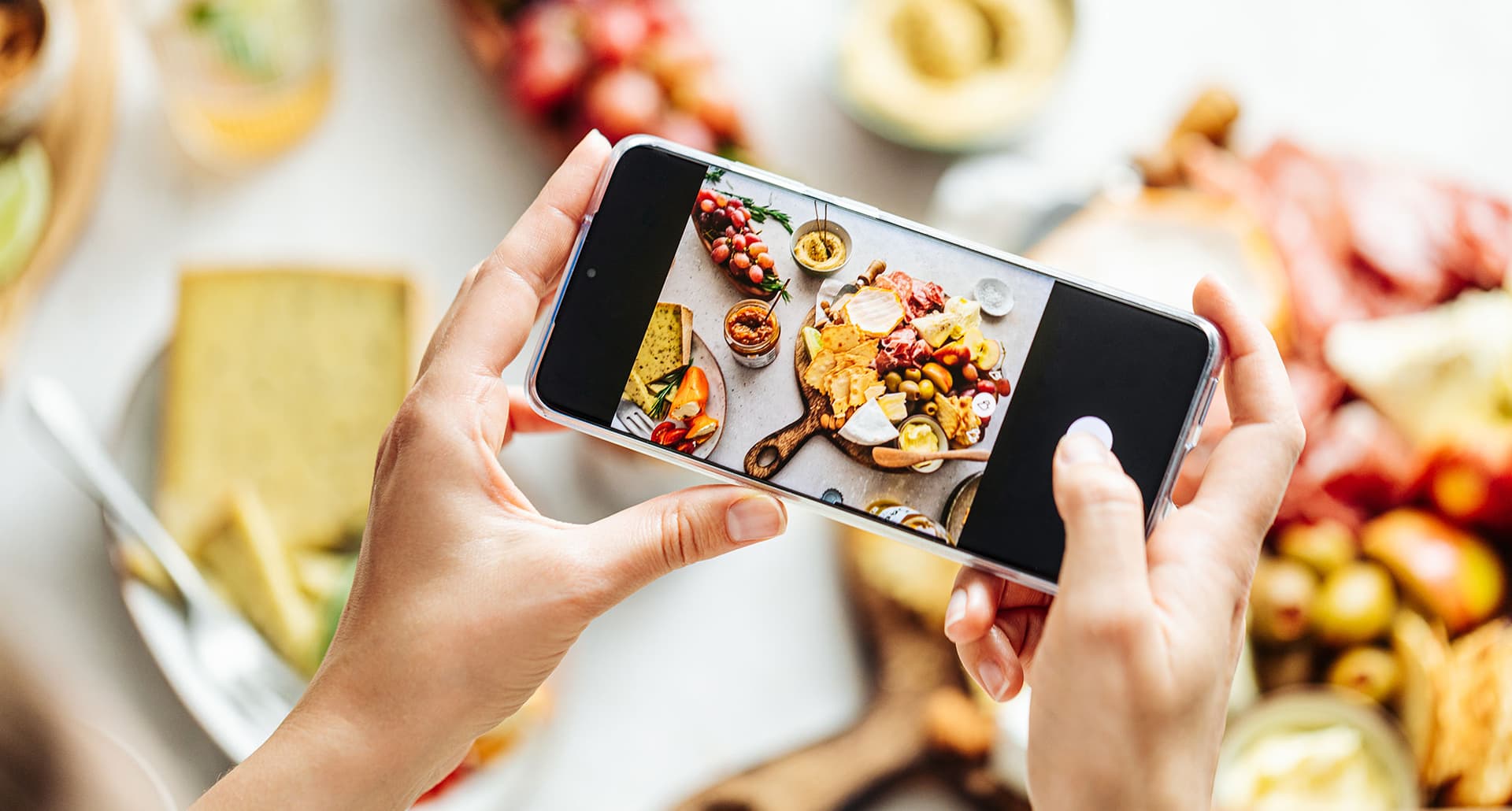 how to take better food photos: hands taking a photo of a mezze spread on a table
