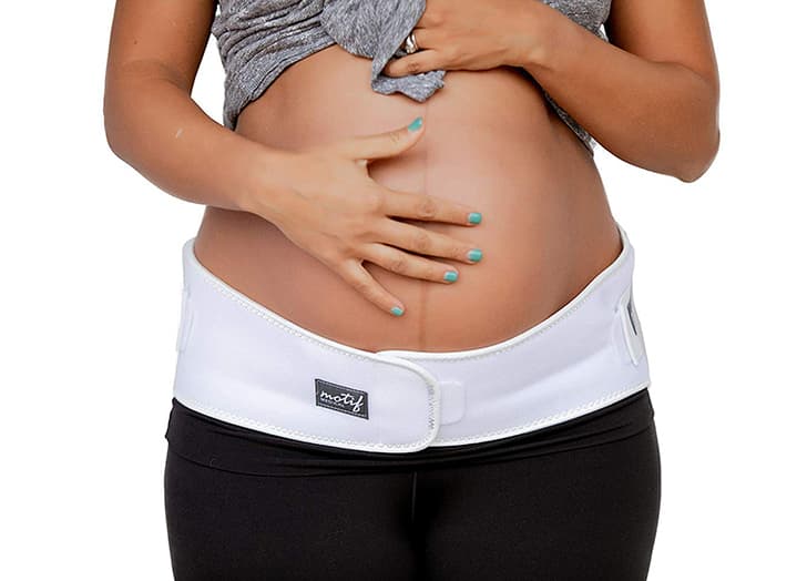 Motif Medical pregnancy support band review: A woman holds her pregnant belly while wearing a band