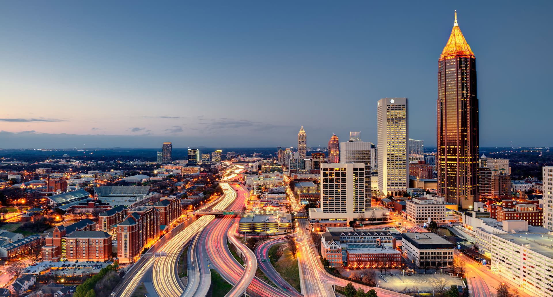 Best Roadtrips From Atlanta - The Atlanta skyline just after sunset. Bright lights, tall buildings, and winding highways fill the frame.