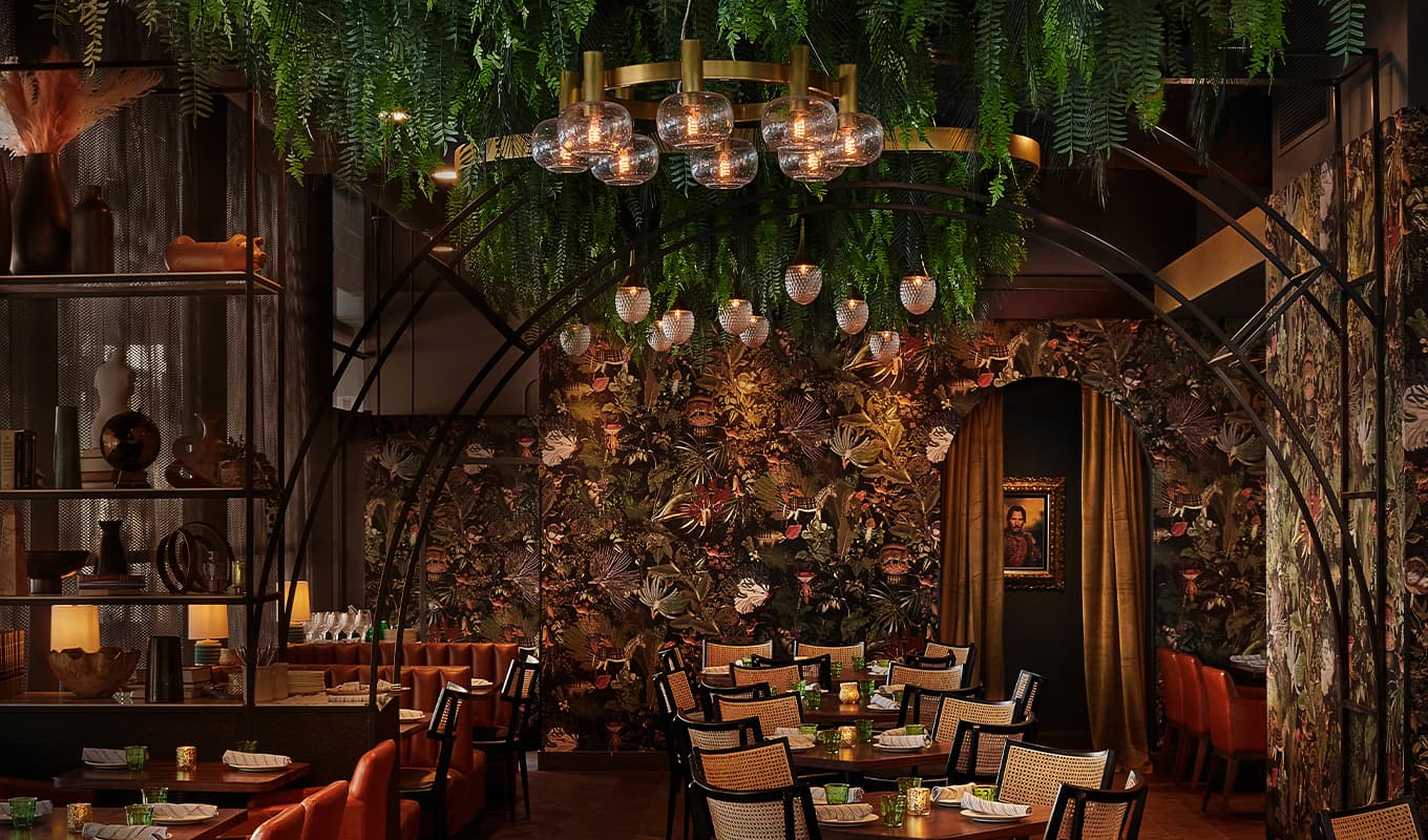 Most romantic restaurants Chicago: A dimly lit restaurant with dark floral wallpaper and greenery overhead