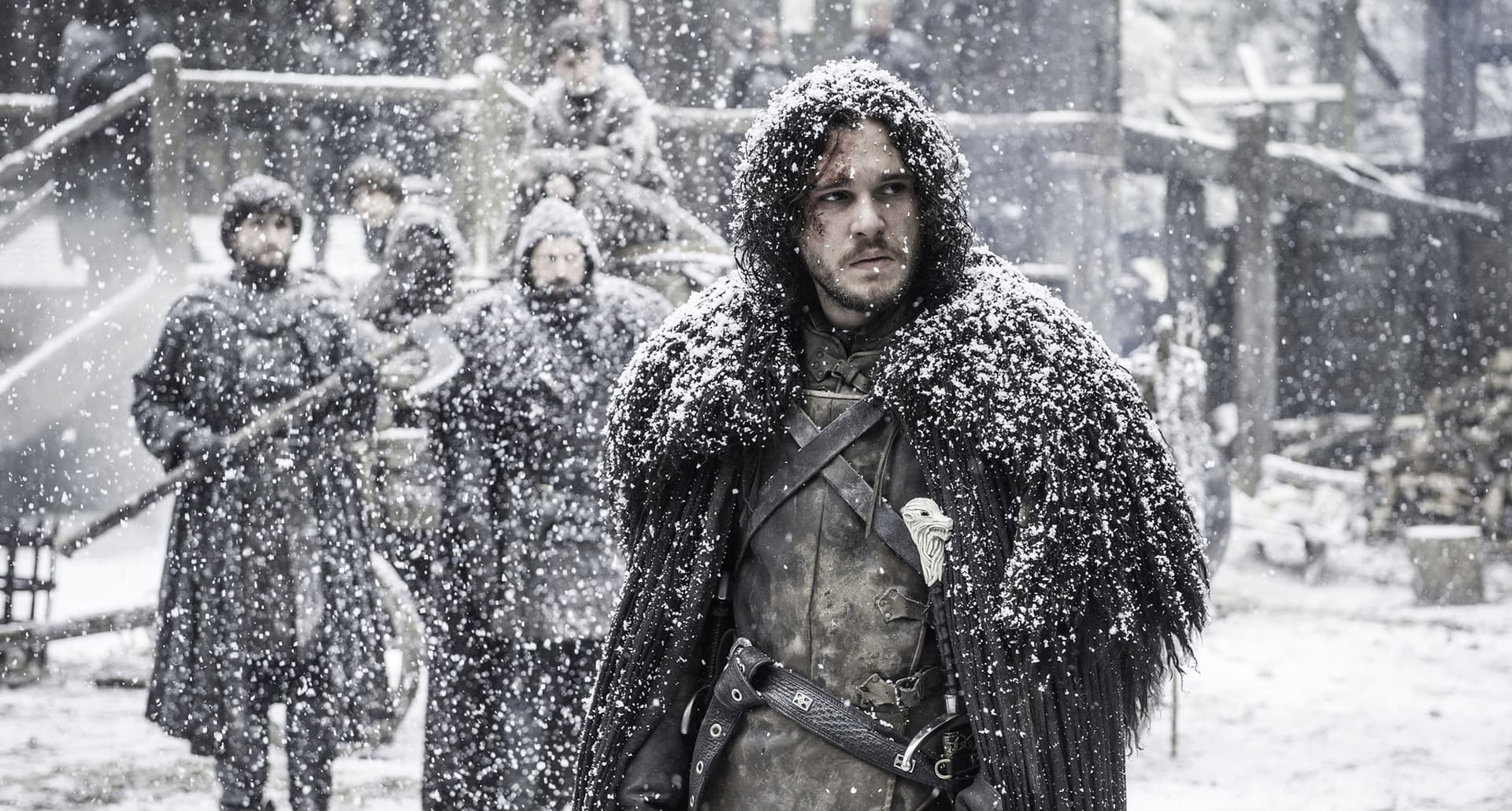 Game of Thrones Seasons Ranked - John Snow up at the wall dressed for winter and covered in snow. He looks concerned and there are fellow men from The Wall behind him.