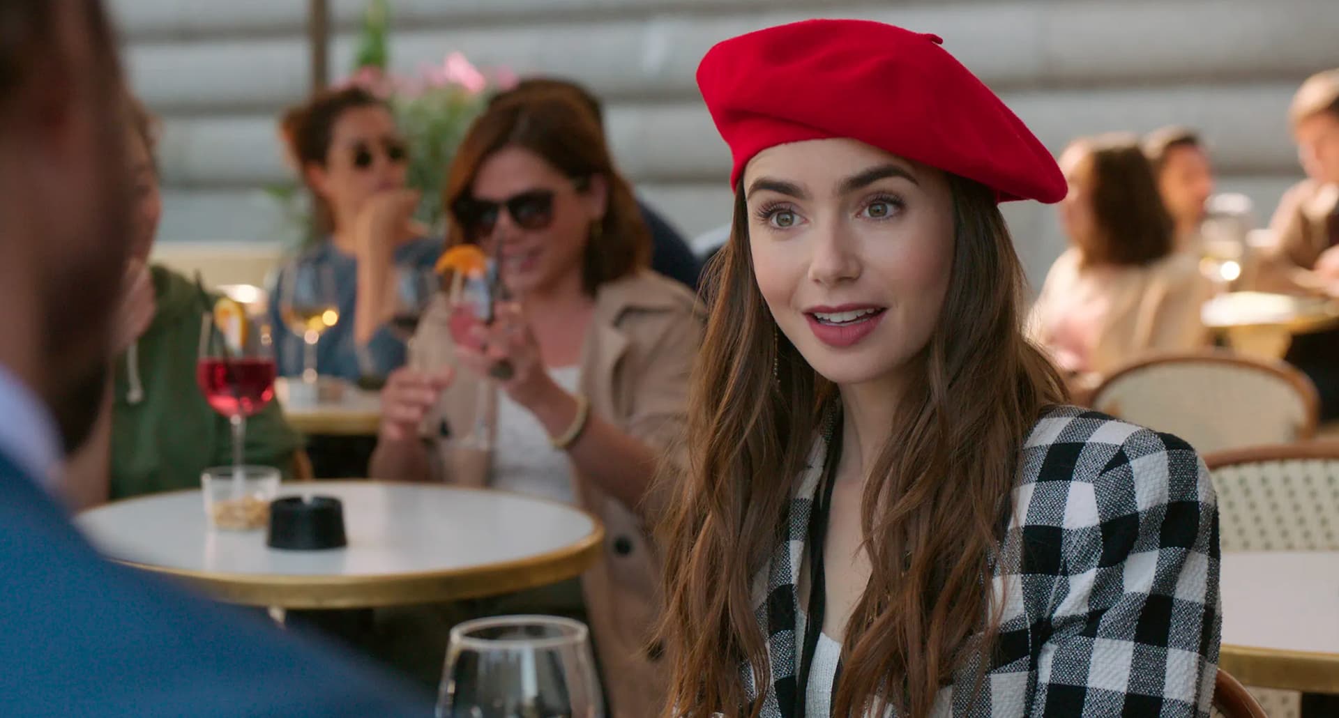 A still from Emily in Paris with Emily at a cafe wearing a red beret.