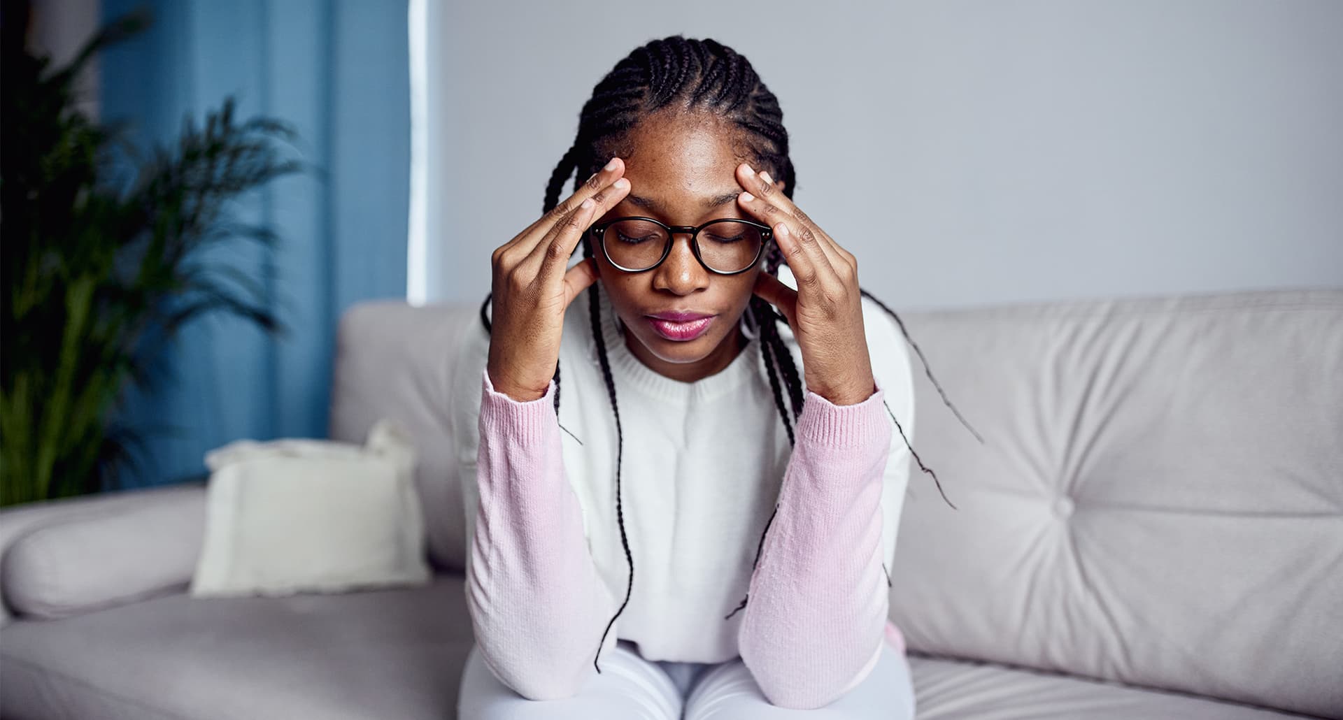 Distressed woman touches her temples while sitting on couch