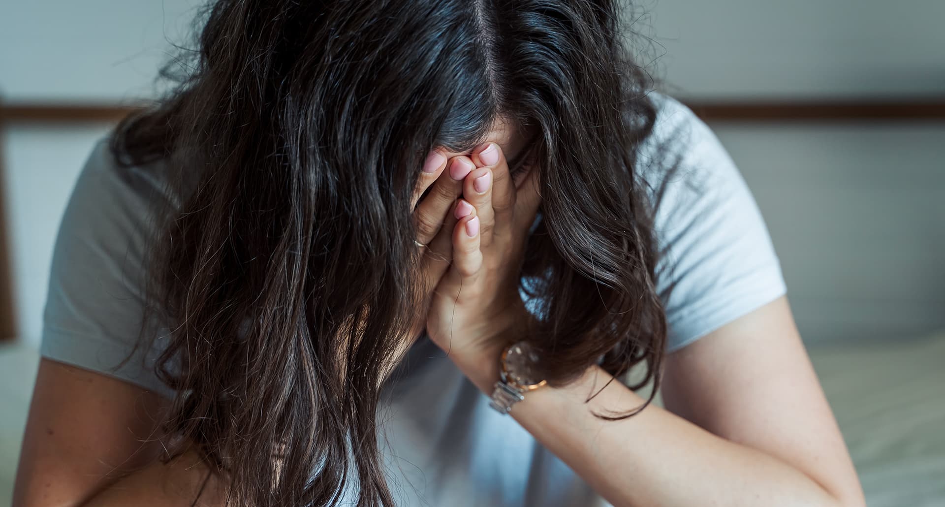 Woman in white tee and short brown hair has hands in her face, clearly upset.