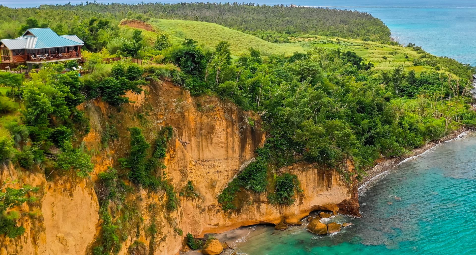 Nonstop Flights from Miami - A house resides on the top of a cliff that overlooks the ocean in Dominica.