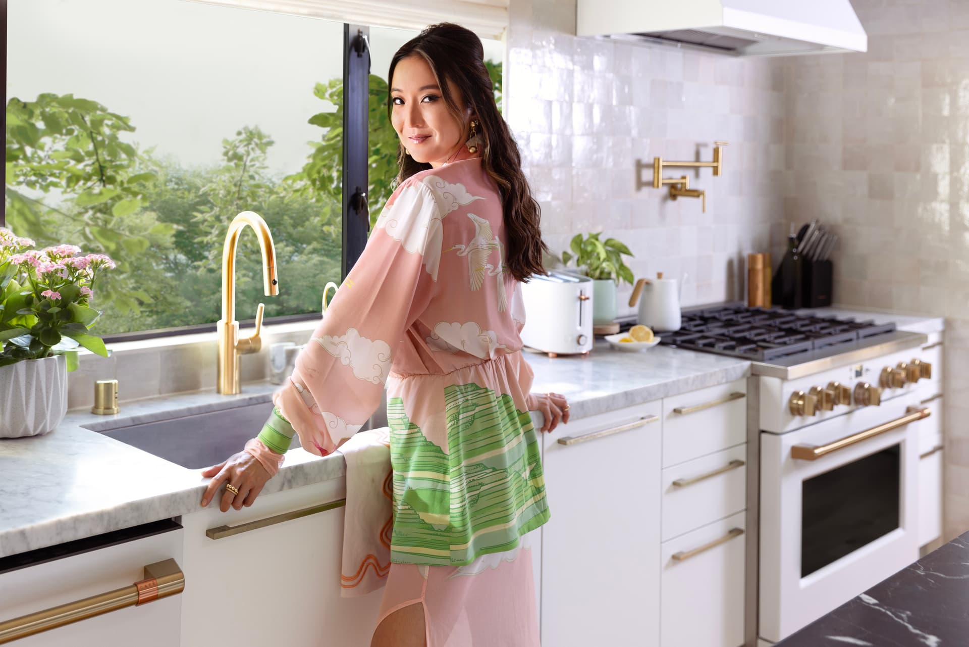 Actress Ashley Park standing in her newly designed CAFÉ kitchen, leaning over the sink.