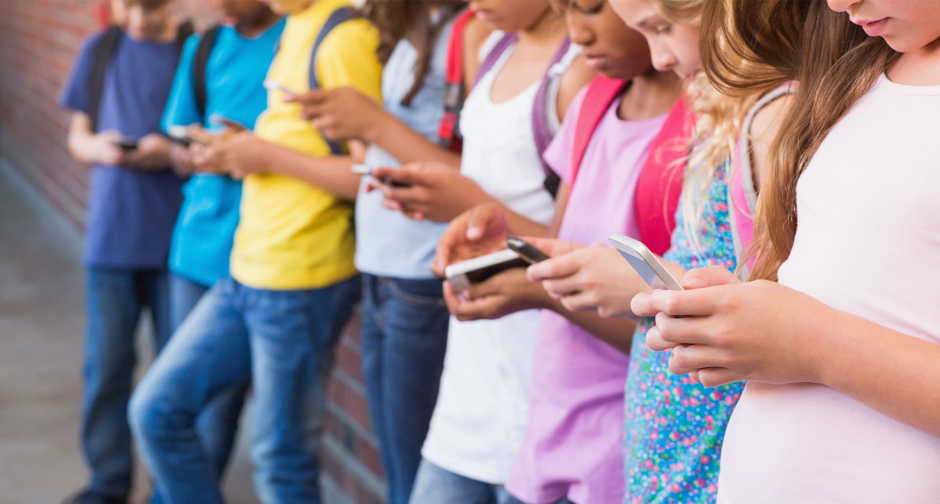 Should-Kids-Have-Cell-Phones-Debate: A group of young children all using cell phones. CLose up on the hands, no face visible.
