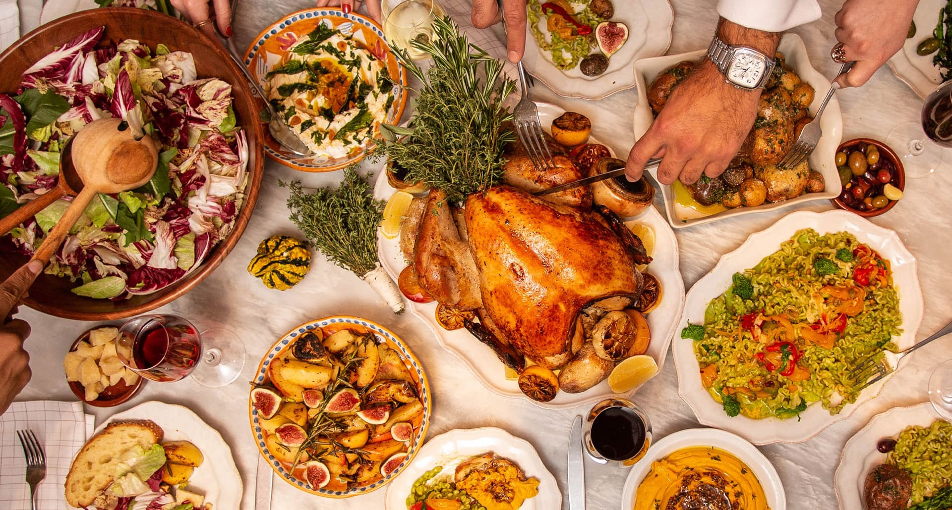 NYC Restaurants Open On Thanksgiving - A large Thanksgiving table spread from Leuca featuring classics like turkey, potatoes, and more. Hands are reaching into the frame to handle the dishes.