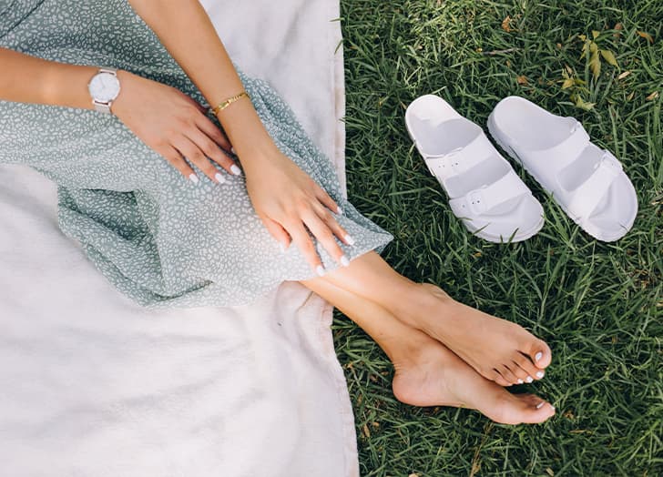 A woman shows off her feet in the grass as her sandals sit beside her.
