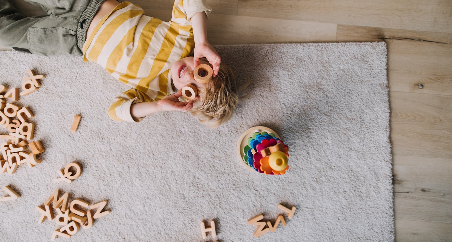 Is My Child Ready for Kindergarten: Overhead view of cheerful small boy playing with wooden toys at home.