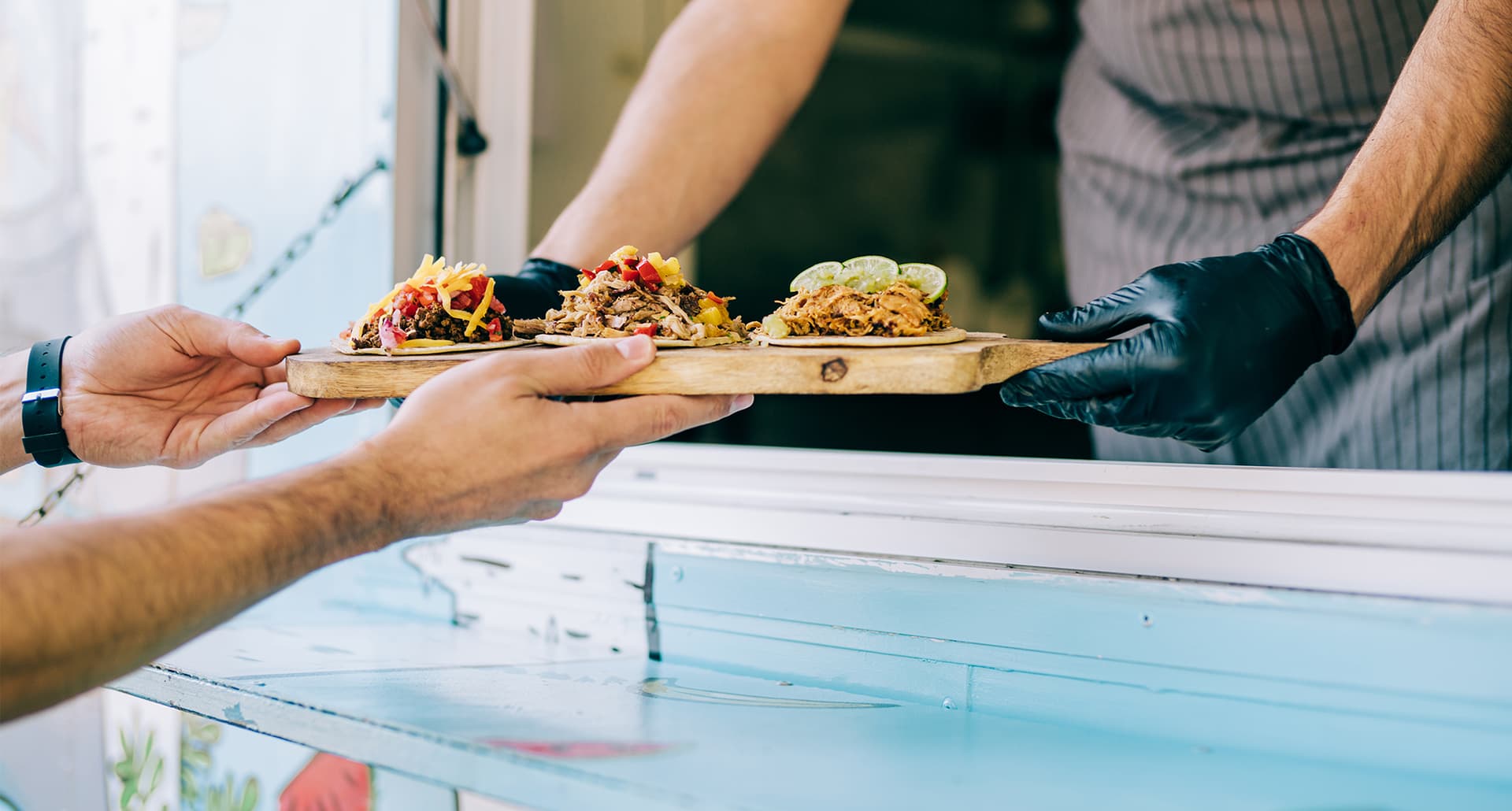 Best Cheap Eats in Los Angeles: Cropped shot of young chef serving tasty tacos to male customer from the window of his food van.