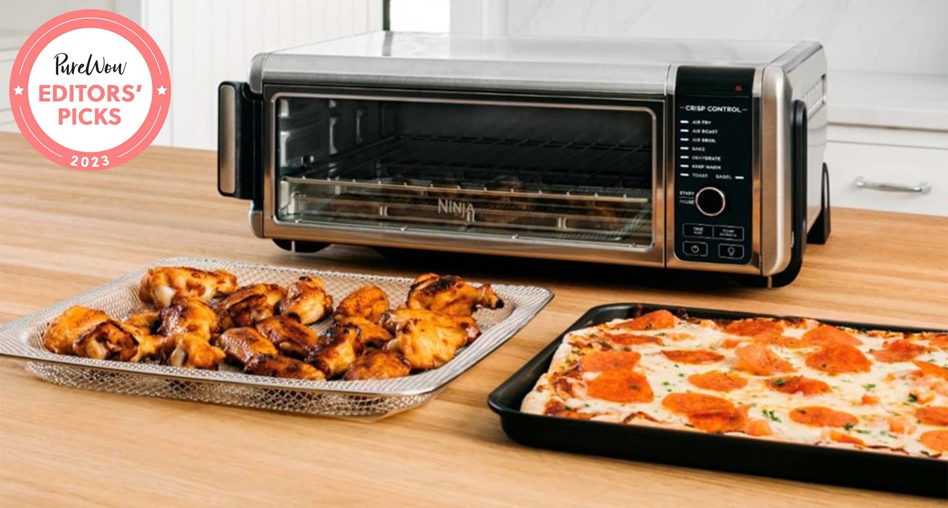 Best toaster ovens: A black and stainless-steel toaster oven behind a rack of chicken wings and a square pizza