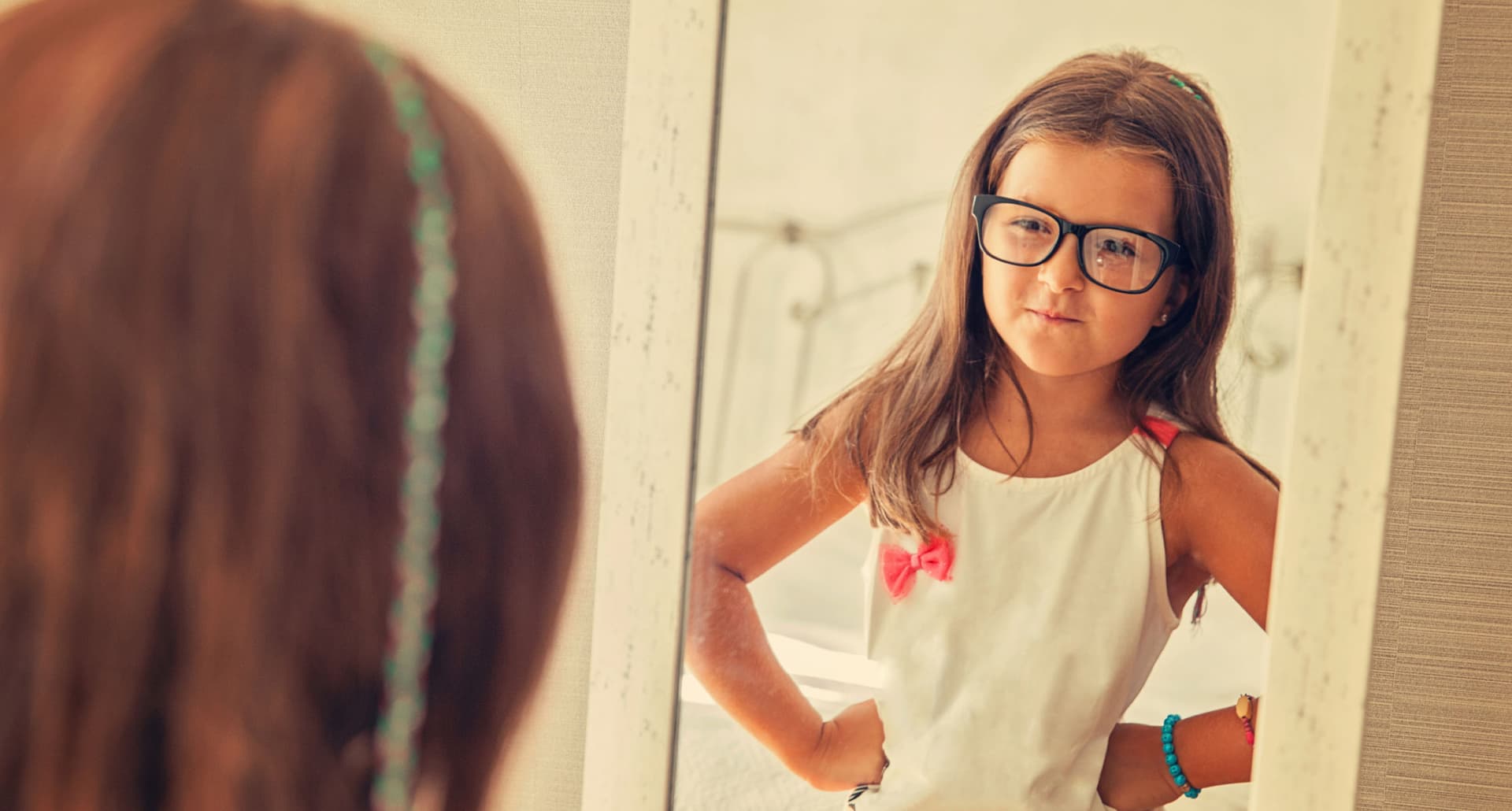 how-to-raise-confident-kids: A little girl looks confidently at herself in the mirror.