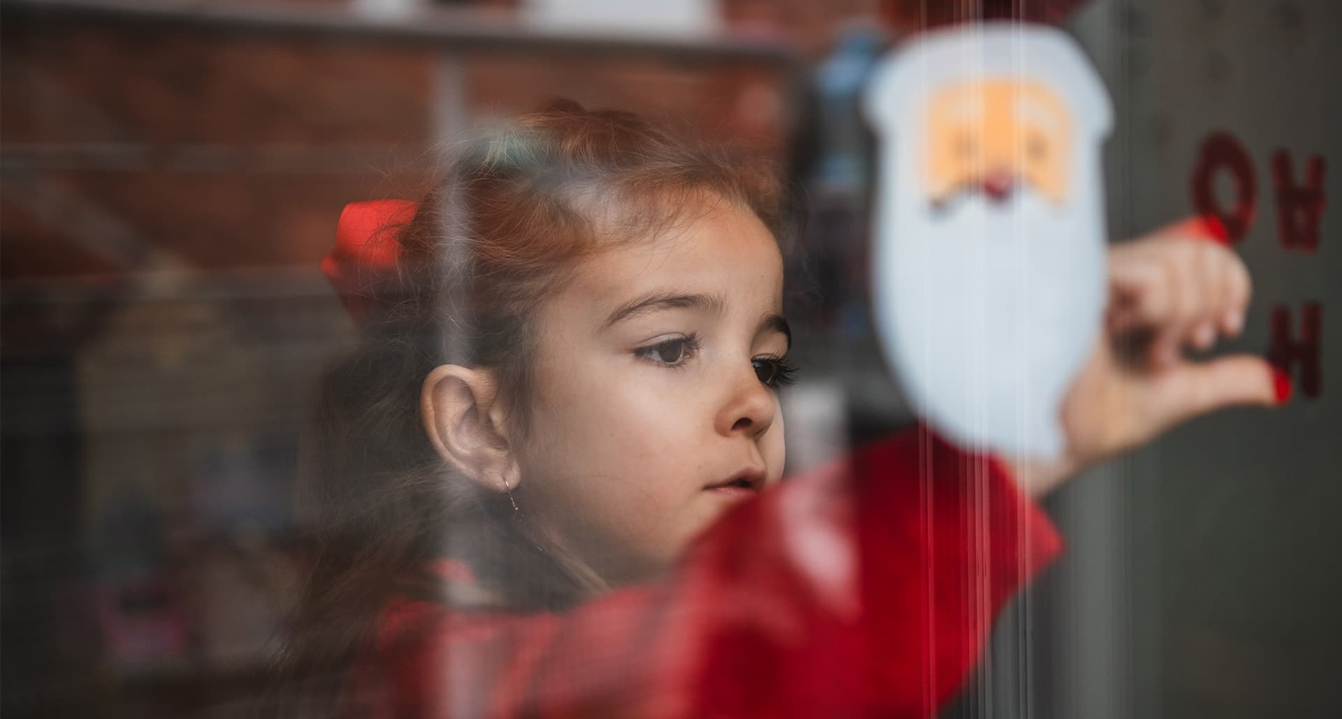 Little girl looks through Christmas decorated window